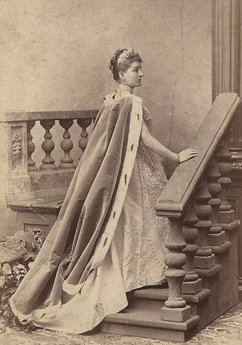 XIX a. pabaigos ateljė fotografija: aristokratė ilga iškilminga apsiaustu prie laiptų turėklų
