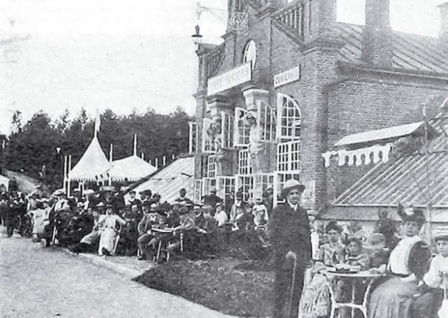 Kavinė „Café Riviera“ Lentvaryje Senos nuotraukos fragmentas: prie mūrinio kavinės pastato prie staliukų sėdi daug elegantiškai apsirengusių lankytojų, šalia palapinė