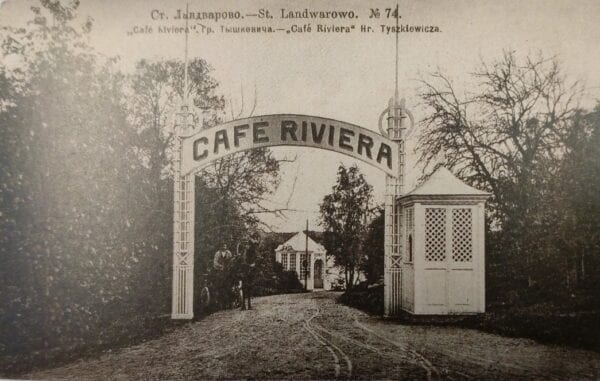 Kavinės „Rivjera“ vartai Lentvaryje Senas atvirukas su arka „Cafe Riviera“ prie kelio, sargo būdelė, medžiai, žmonės tolumoje