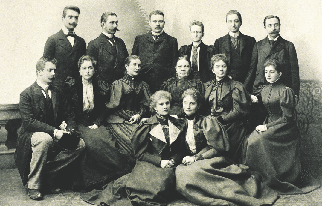 Senovinė grupinė fotografija: keturiolika XIX a. pabaigos aprangos vyrų ir moterų pozuoja ateljė